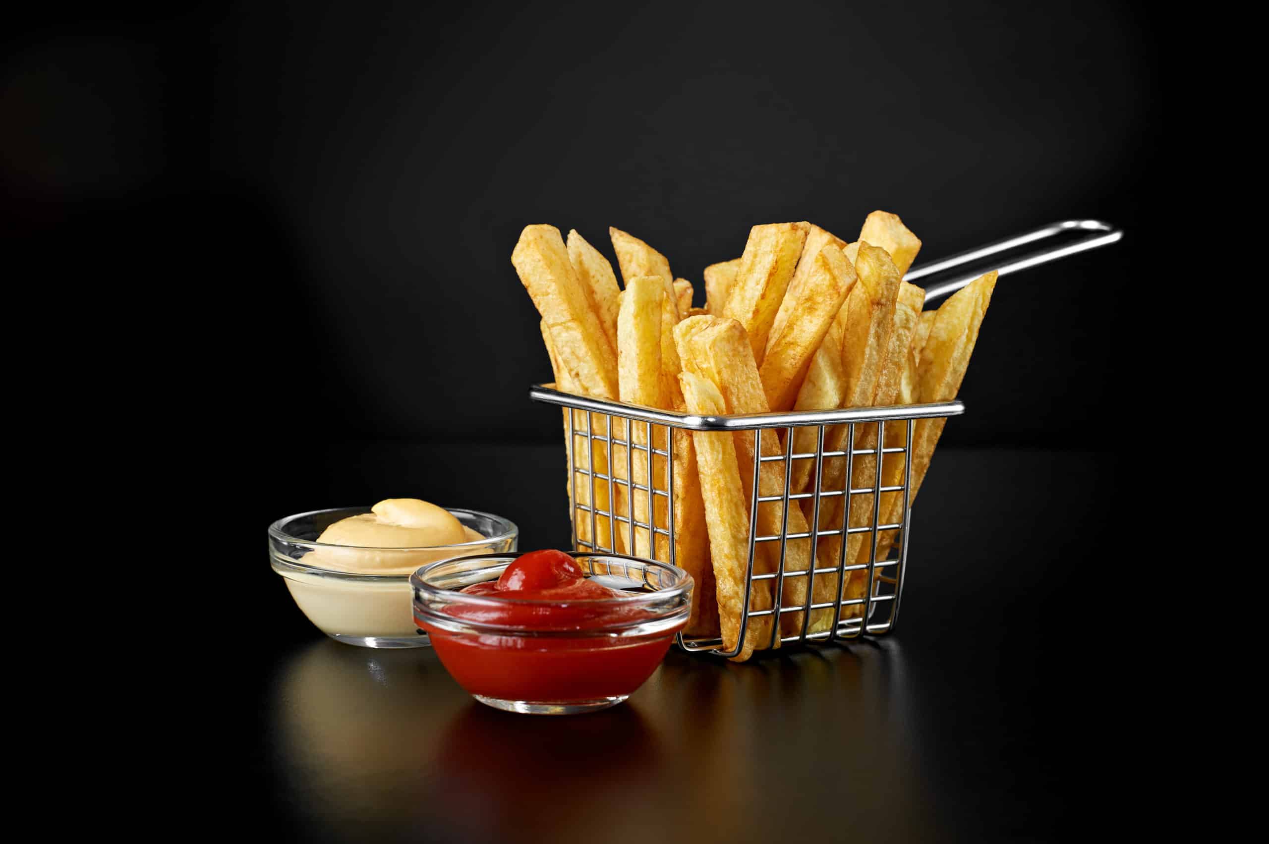 French fries in basket with ketchup and sauce isolated on black