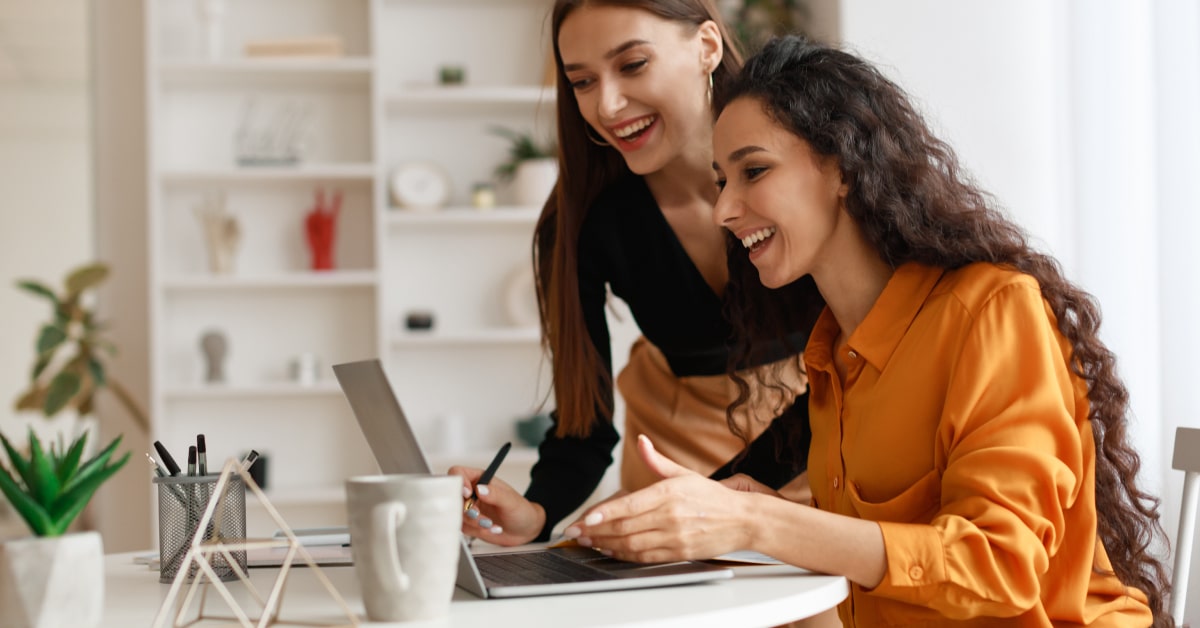 Featured image for "Want to Drive More Staffing Sales? Change How You Write!" blog post. Two woman are looking and smiling at a computer screen.